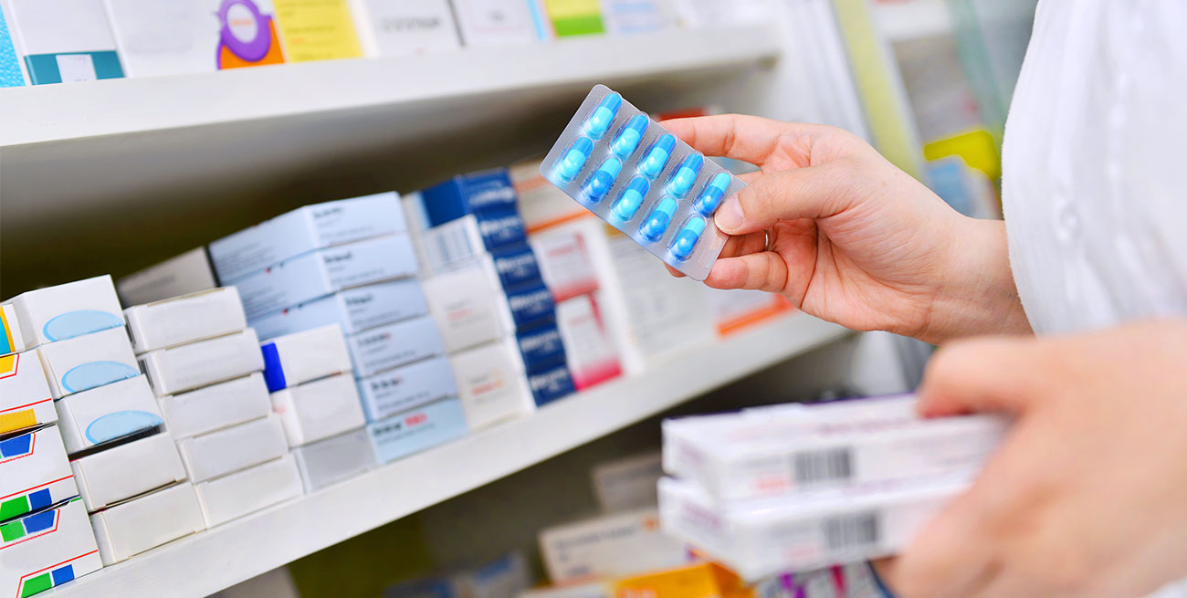 Farmacêutica segura cartela de medicamentos azuis na frente de prateleira de remédios