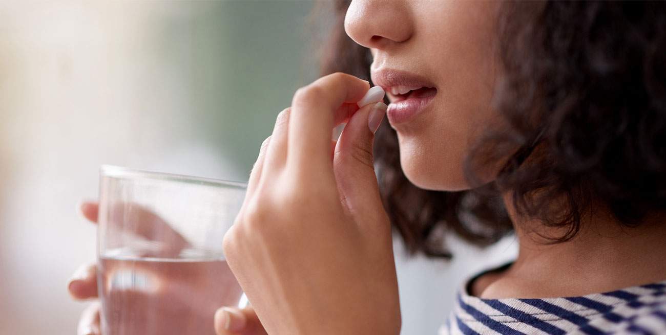 Mulher toma medicamento em comprimido e segura copo de água
